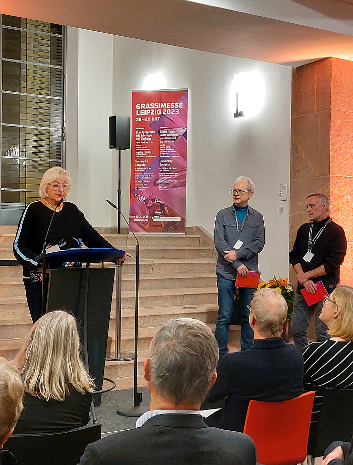 smow co-founder Martina Stadler reads the laudatio for Cornelius Réer (m) Annabella Hevesi / Line and Round IO (l, represented by Gabor Bella) at the opening of the 2023 Grassimesse Leipzig